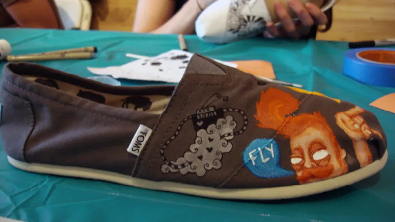 A close up of a TOMS loafer has a bracelet and a person who is saying “fly”.