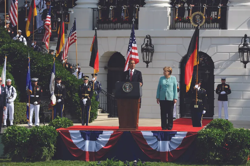 A photo of Barack Obama speaking outside the White House. Standing next to him is Angela Merkel.
