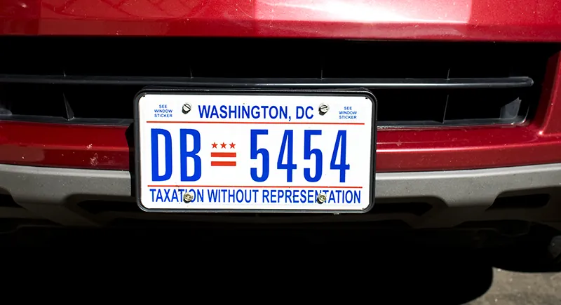 A Washington, DC license plate on the front bumper of a car reads: Washington, DC with the number DB 5454 written in the middle. Taxation Without Representation is written at the bottom.
