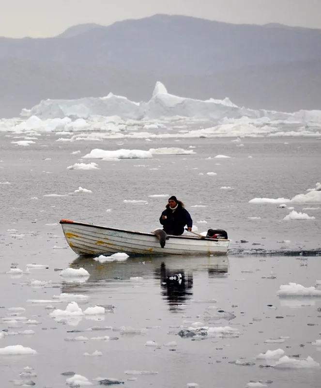 A lone man steers a small motorboat through ice-strewn water.