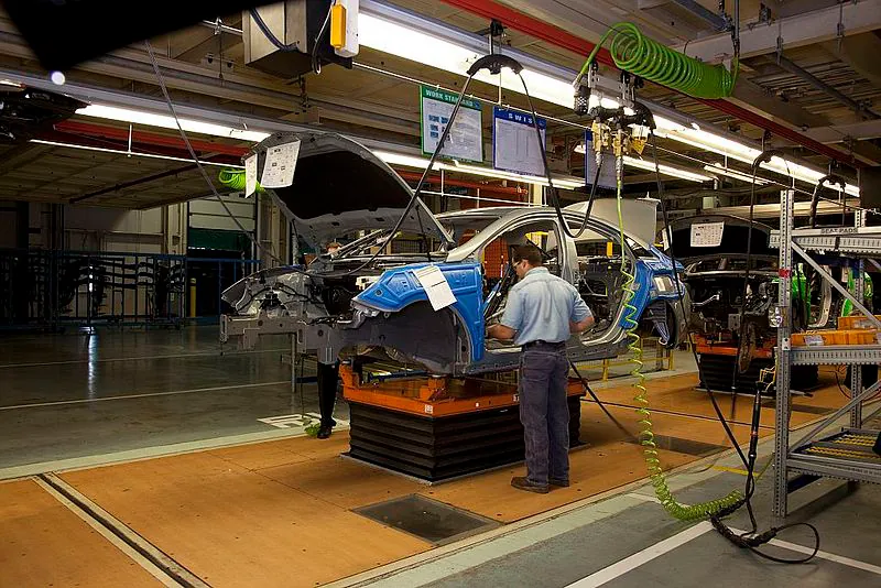 A man is shown using a machine to install car parts on an assembly line.