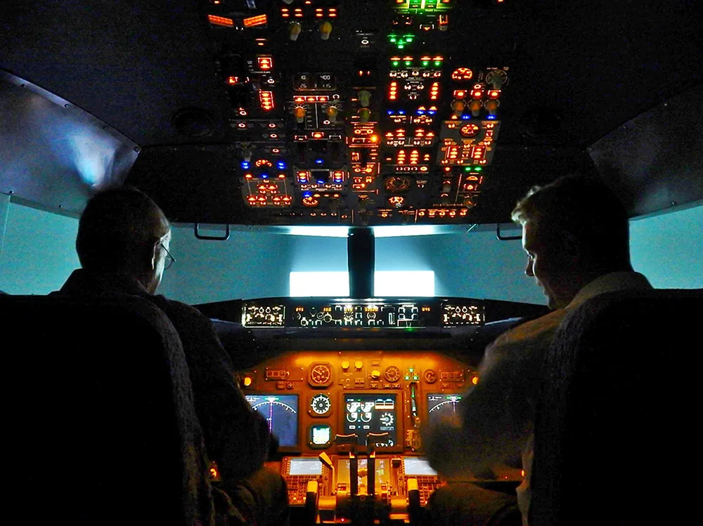 A photo shows the rear view of a flight instructor describing various dials and displays to a trainee pilot in the cockpit of a Boeing 7 3 7 simulator.