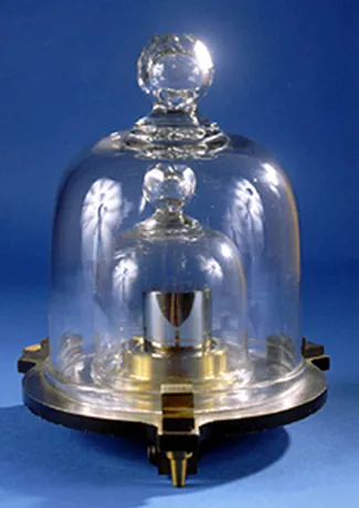 La foto muestra un pequeño cilindro de metal sobre un soporte. El cilindro está cubierto por 2 tapas de cristal, con la tapa de cristal más pequeña encajada dentro de la tapa de cristal más grande.