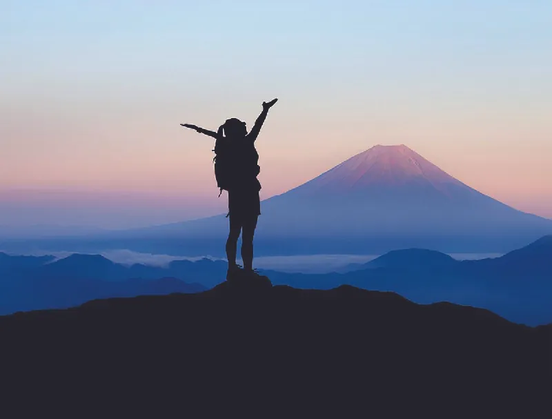 Photo of a hiker at the top of a hill, looking out at a mountain.