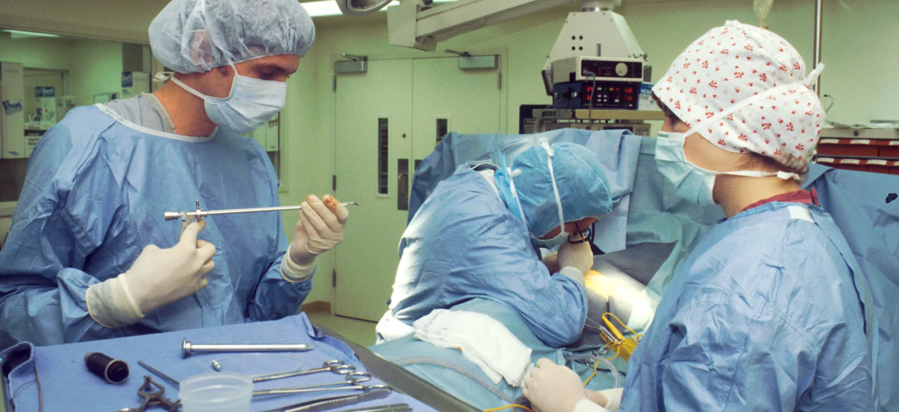 Three medical professionals wearing personal protective equipment prepare instruments in an operating rooms.