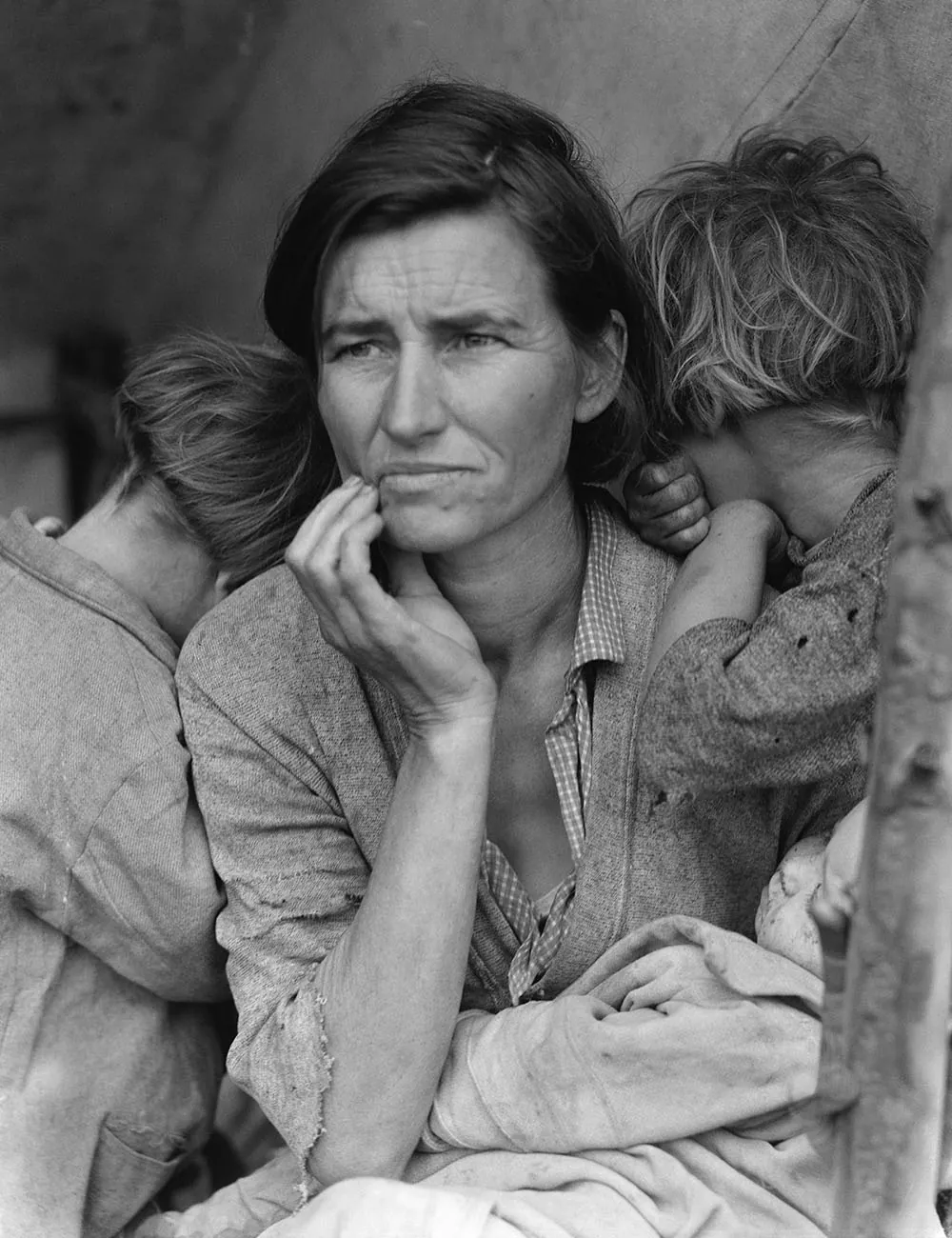 A black and white photo shows a desperate-looking woman sitting with two children who bury their faces against her shoulders.