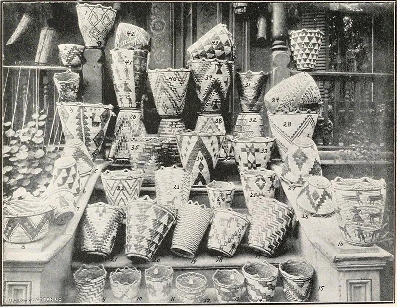 Collection of approximately 40 baskets arranged on the steps and banisters of a porch. They display a variety of shapes, patterns, and construction techniques.