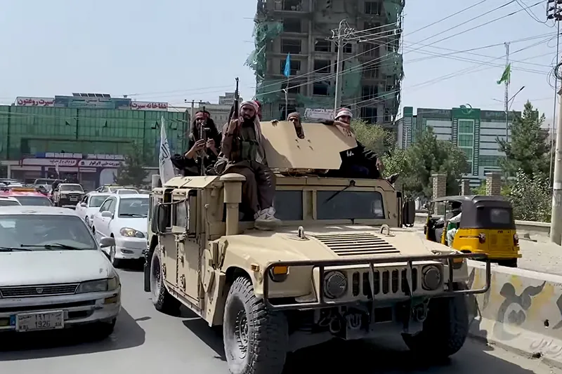 Taliban fighters sit on top of a Humvee, driving with other traffic in Kabul.
