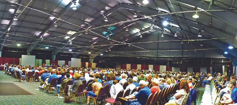 An image of a large group of people sitting in chairs inside of a large room.