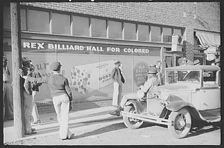 A group of black men and an old car standing outside a billiard hall.