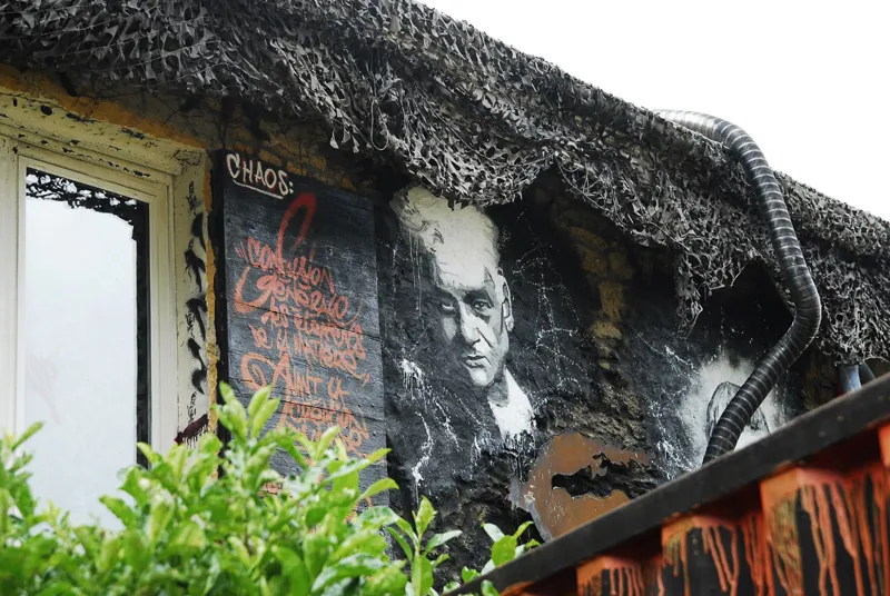 Painting of Jacques Derrida on a building, along with other graffiti art.
