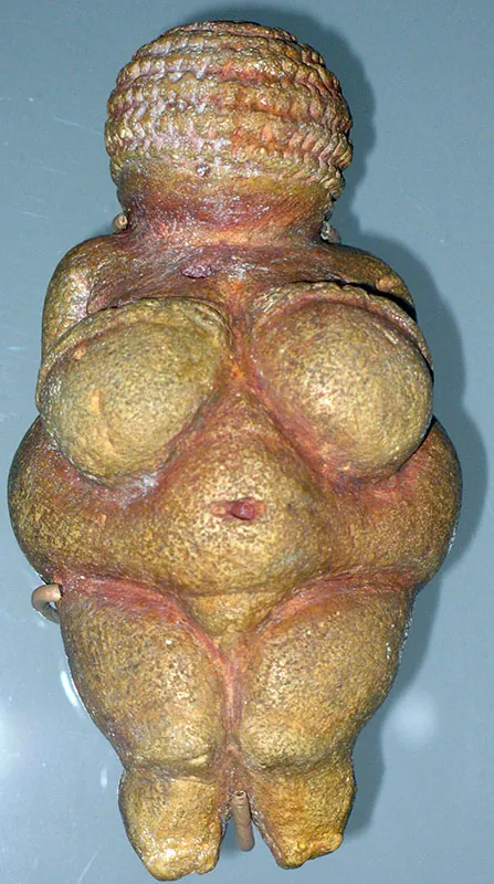 Small stone figurine with a woman’s body. Figurine has large breasts and a round belly.