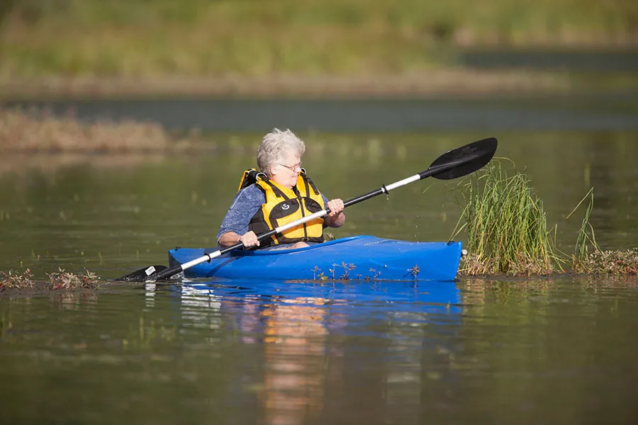 An older person paddles a kayak.