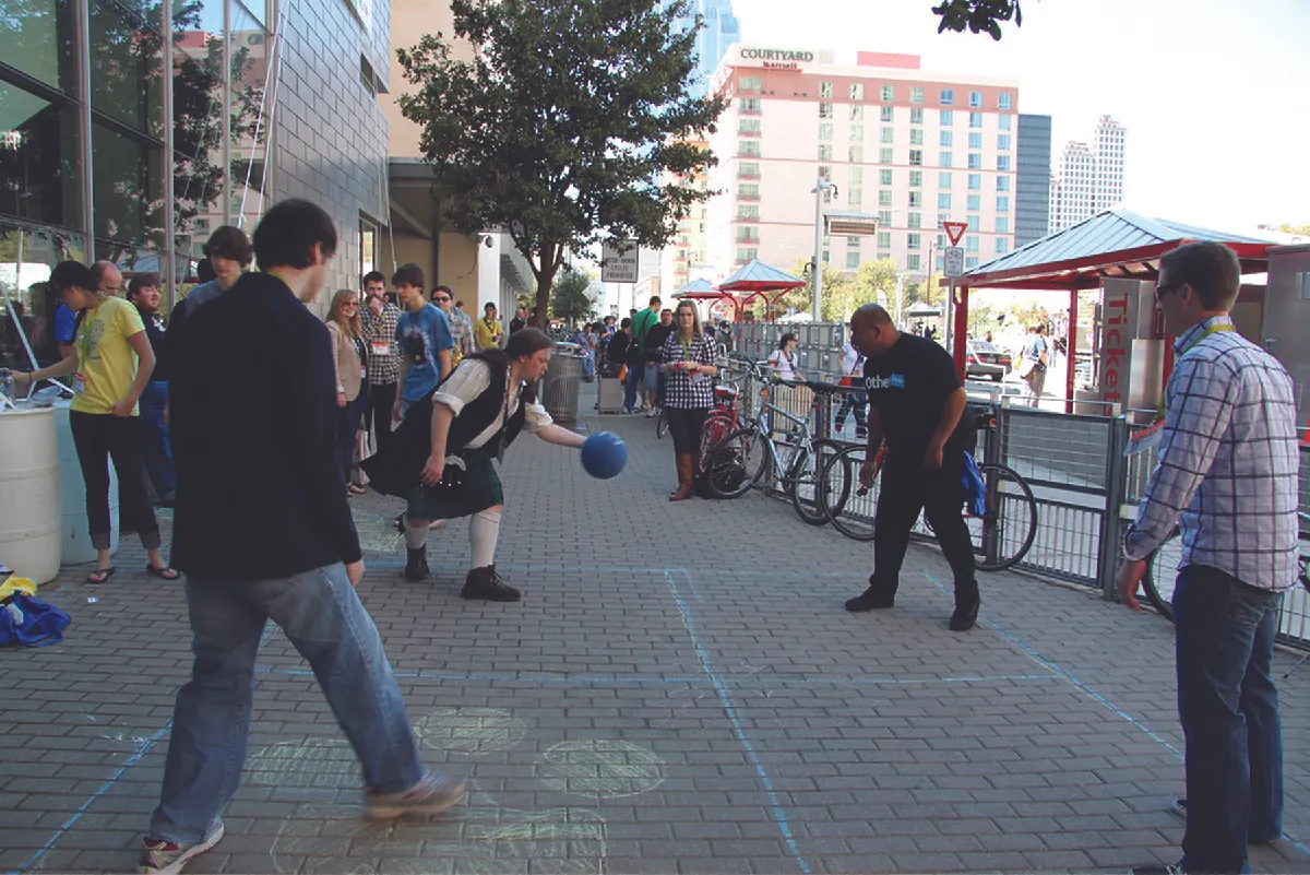 People playing a game of foursquare on a brick sidewalk.