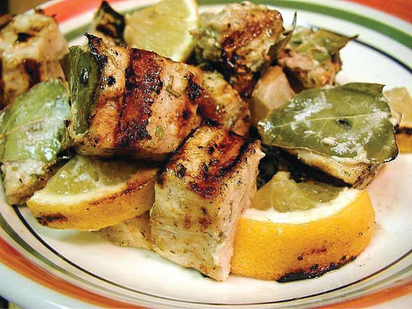 Grilled swordfish is displayed with grilled vegetables and oranges on a plate.