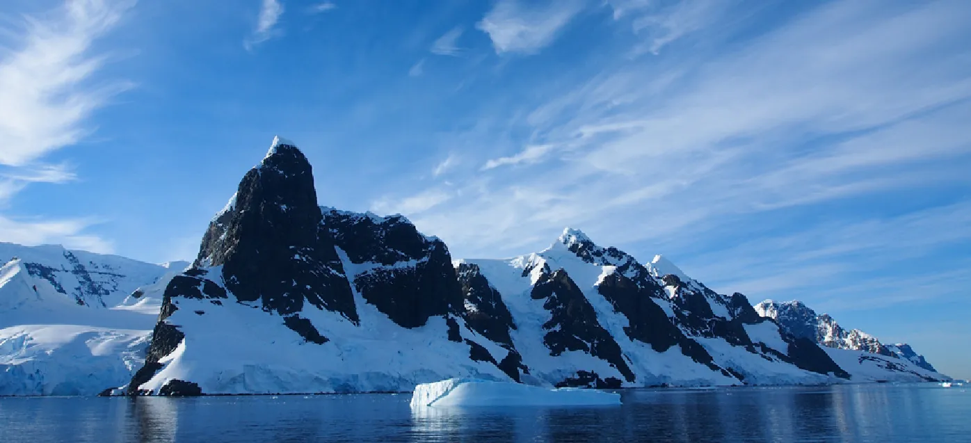 Picture of Antartica showing water, mountain, and iceberg peaks under a bright blue sky