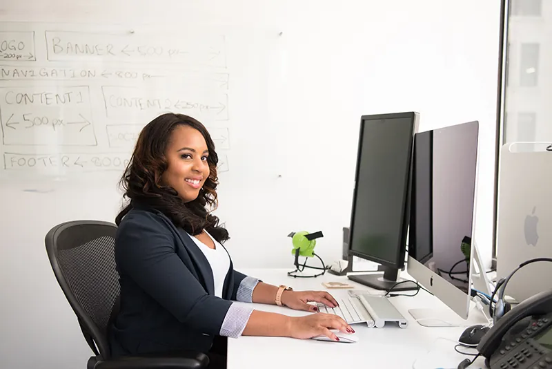 A worker sits at a desk in front of multiple computer monitors and a phone.
