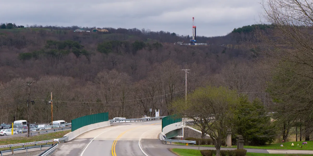 A photograph shows a rural landscape, and on the hill in the distance is a large, high tech drill.