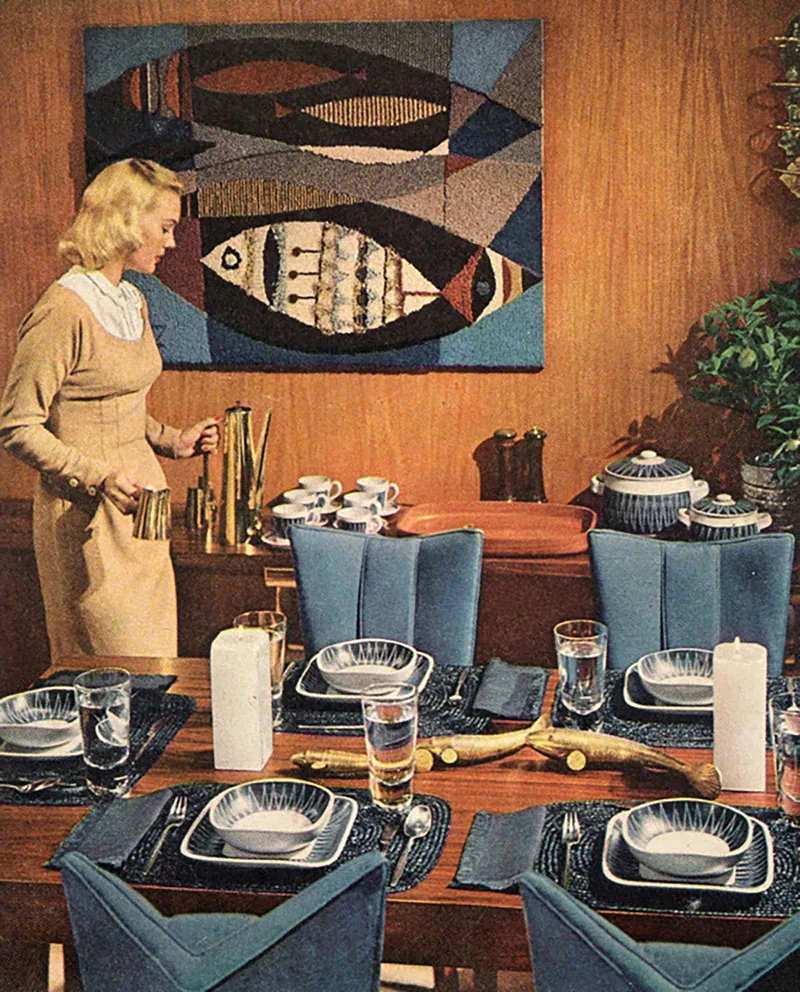 Woman in 1950s or 1960s dress putting coffee on buffet in a formally set family dining room.