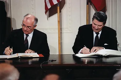 A photograph shows Mikhail Gorbachev and Ronald Reagan sitting beside one another as they sign the INF Treaty.