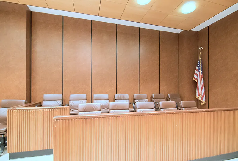 A jury box has 12 chairs for jurors to sit in, seven in the back row and five in the front. An American flag stands in the corner.