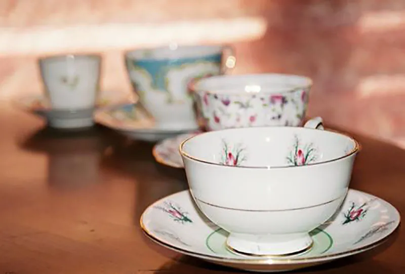 Four porcelain teacups with saucers lined up on a table.