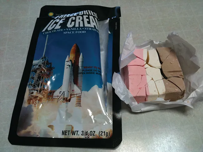 Fotografía que muestra un paquete con un cohete en lanzamiento en la parte delantera y un bloque de sólido a rayas rosas, blancas y marrones en un envoltorio al lado.