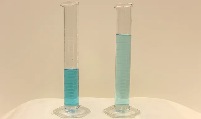 This figure shows two graduated cylinders side-by-side. The first has about half as much blue liquid as the second. The blue liquid is darker in the first cylinder than in the second.