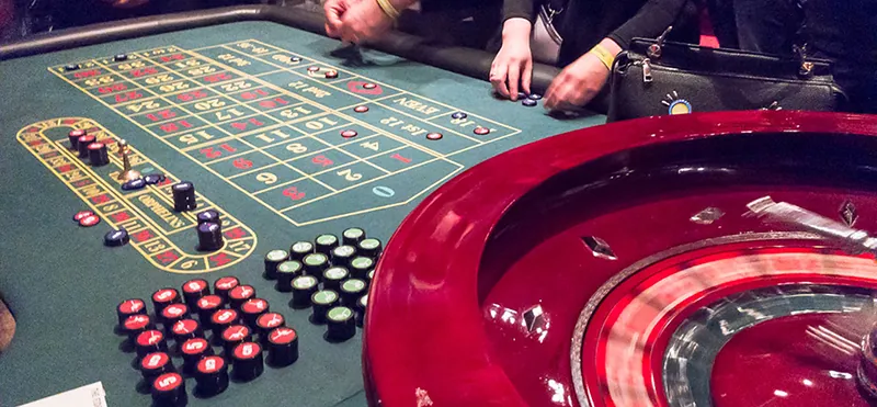 A game of roulette is in progress. Players have placed chips over numbers on the board. The wheel is spinning.