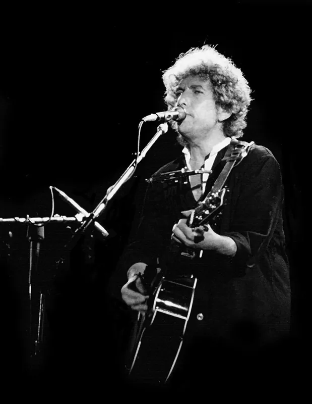Bob Dylan singing and playing guitar during a concert.