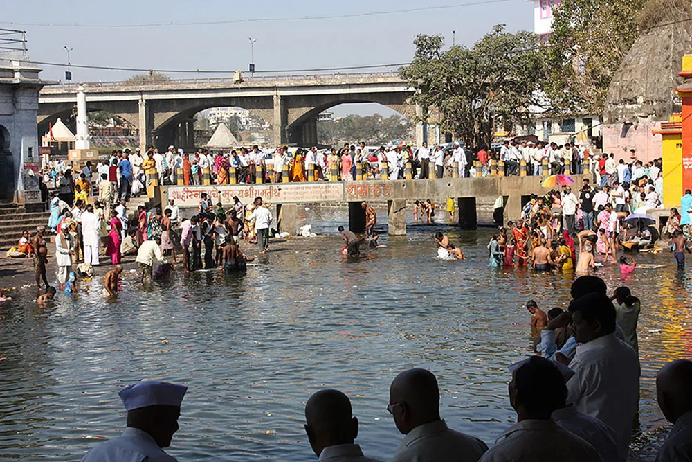 A large group of people surround a body of water. Several people are in the water.