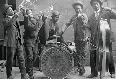 A photograph shows a group of Black jazz musicians playing their instruments. A drum reads “Jazzing Orchestra / King and Carter / Houston Tex.”