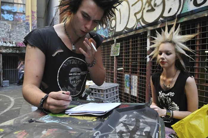 Two people with extremely spiked hair stand at a table in what looks like a studio.