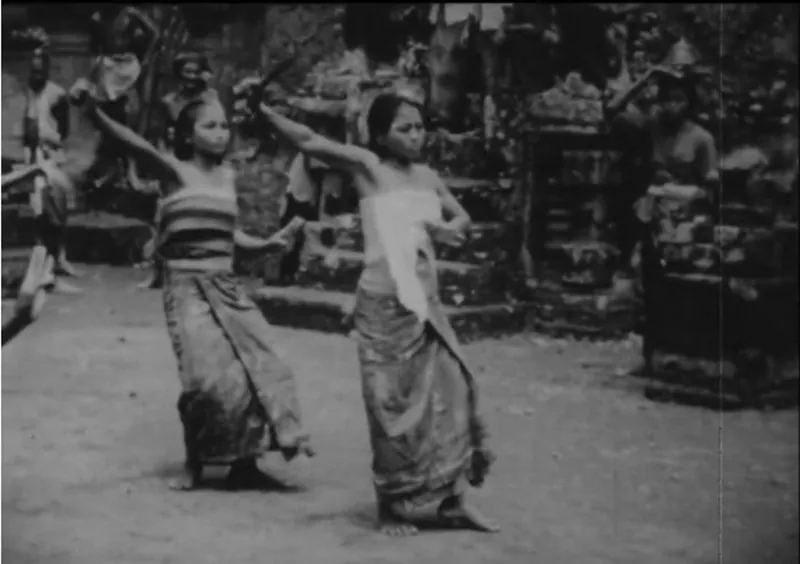 Frame from a black-and-white film of two young girls wearing wrap skirts and performing dance moves in unison.