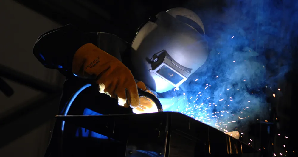 Photograph of a welder wearing protective gloves and helmet, engaged in the task of welding.
