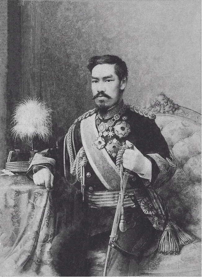 A portrait of a man with a moustache, long pointy goatee, and black hair in a royal military uniform. There are medals on the front of his coat, a sash, and a belt with tassels. He is sitting on an ornate, cushioned sofa with a feathered hat on a draped table to his right and holding a sword in his left hand. His face shows a serious expression.