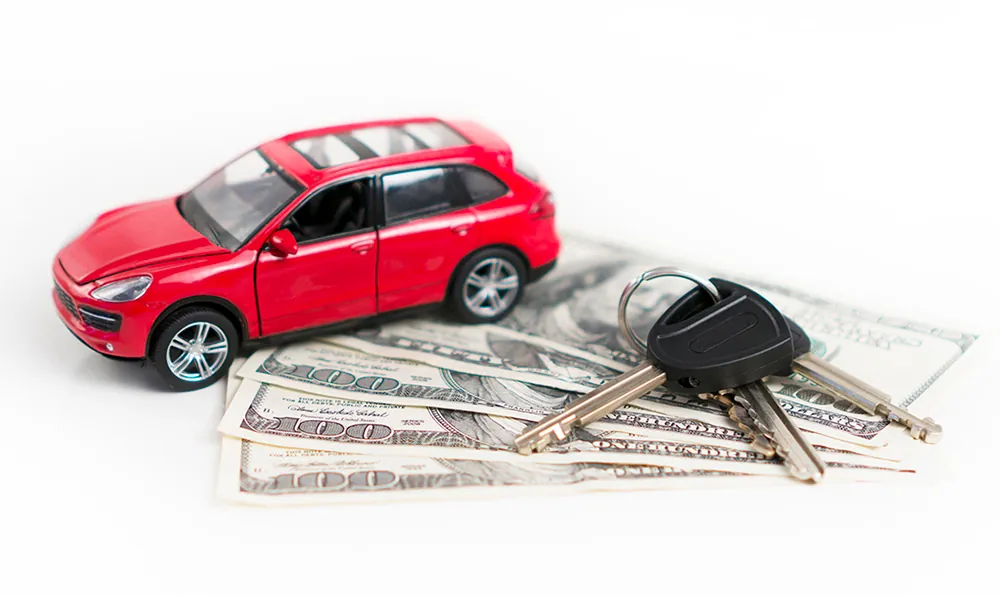 A miniature car is parked on currency notes and keys are placed next to the car.