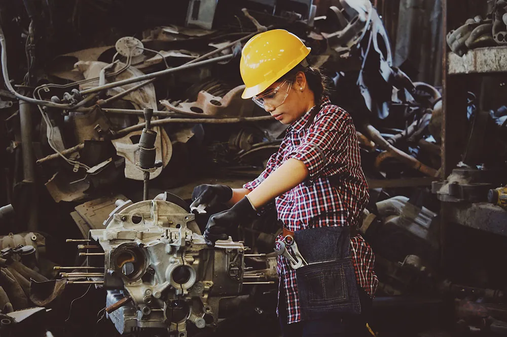 A photo shows a woman wearing safety gear and working on a car part in a factory.