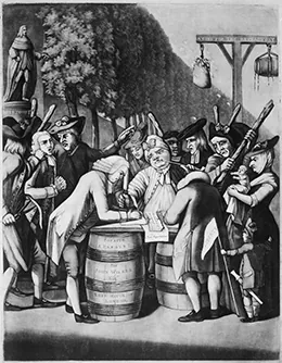 An engraving shows a merchant signing a non-importation agreement outdoors on a makeshift table of barrels, surrounded by a crowd of stern-looking people holding thick sticks. Behind him, another man, forcibly held by a group of threatening-looking men, is apparently next in line to sign the agreement. In the background, a bag of tar and a bag of feathers hang from a wooden structure.