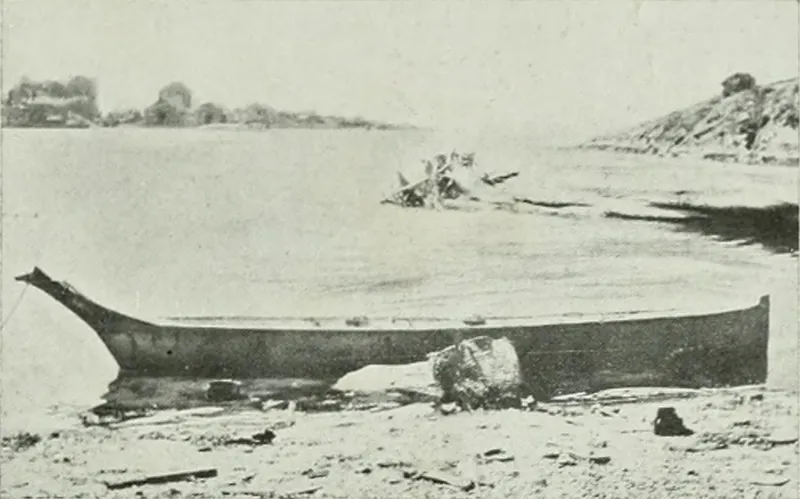 Black and white image of a wooden canoe on a beach.