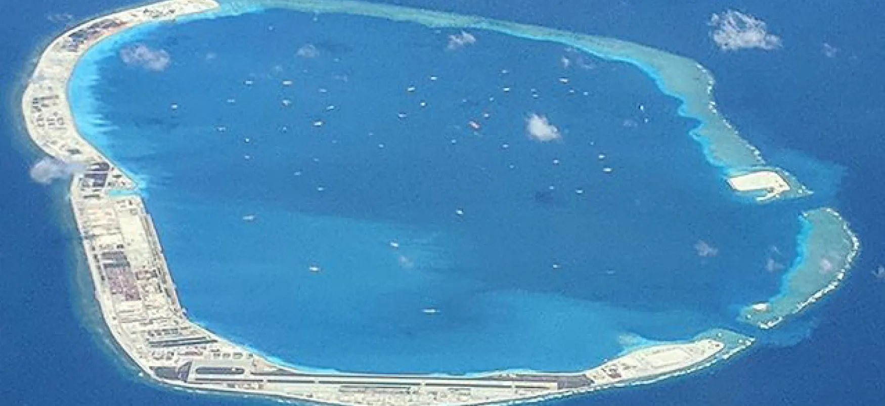 A small man-made island in the South China Sea is seen from above. The island is a narrow ring, with a small inlet allowing water into the interior of the island.