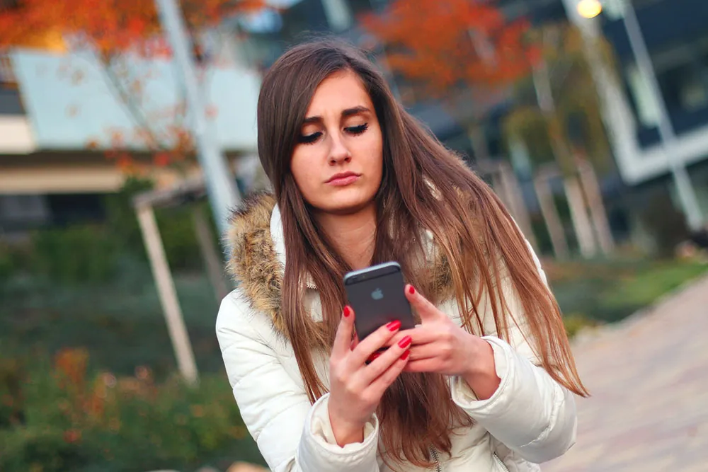 A photo shows a young woman looking at a cell phone.