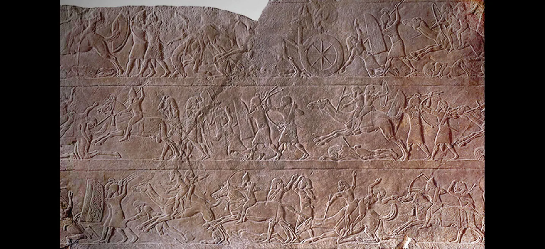 A picture of a piece of brown stone is shown with carvings of three rows of fighting scenes. The top of the stone is broken on the left side and there is a crack running down the middle of the stone. The scenes depict images from combat – people dressed in cloths tied around their waists and elaborate headdresses using shields to protect themselves. Some are fighting with spears, swords, bows and arrows, and some are riding camels and horses with chariots. Some people are laying on the ground or falling.