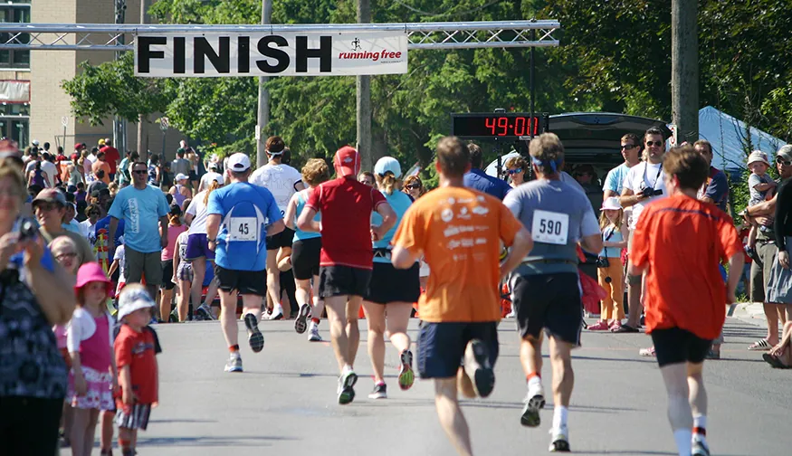 A runner crossing a finishing line on a road with a clock showing his finish time.