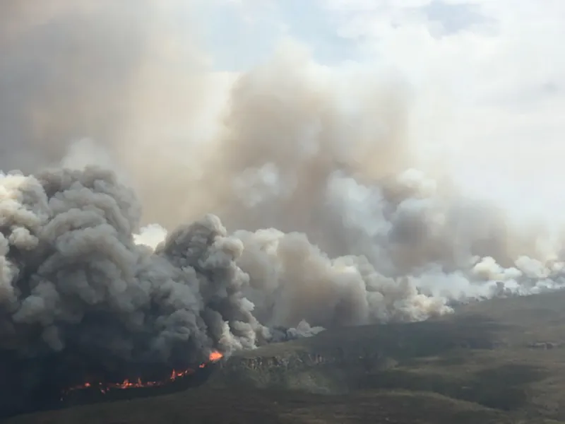 Distant view of the landscape with enormous clouds of smoke rising from fires burning on the ground.