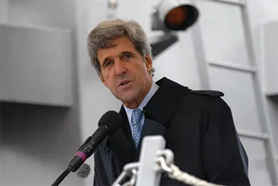 A photograph of John Kerry speaking into a microphone is shown.