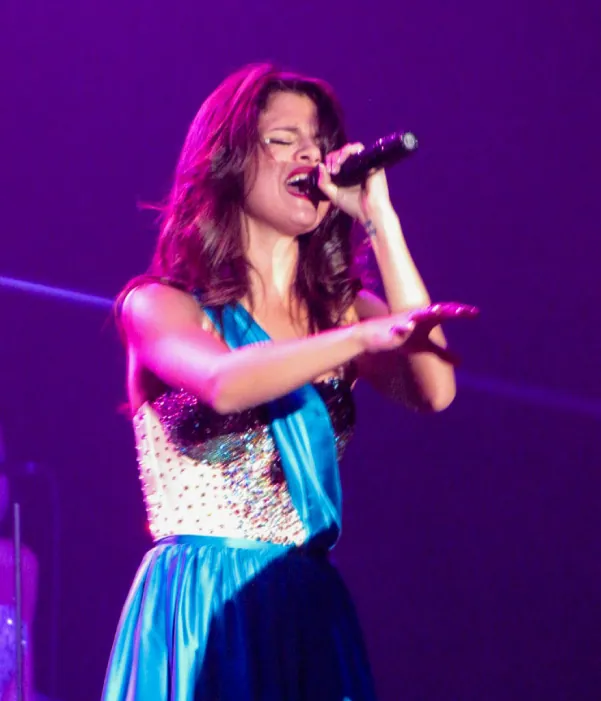 Selena Gomez on stage singing in a sparkly costume.