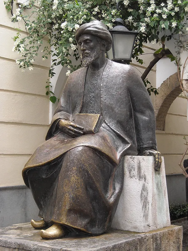 Statue of a seated man wearing a long robe and holding a book in his lap.