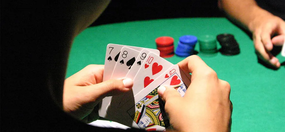 A person is shown holding 5 playing cards. The hand of another player is shown near a pile of plastic chips.