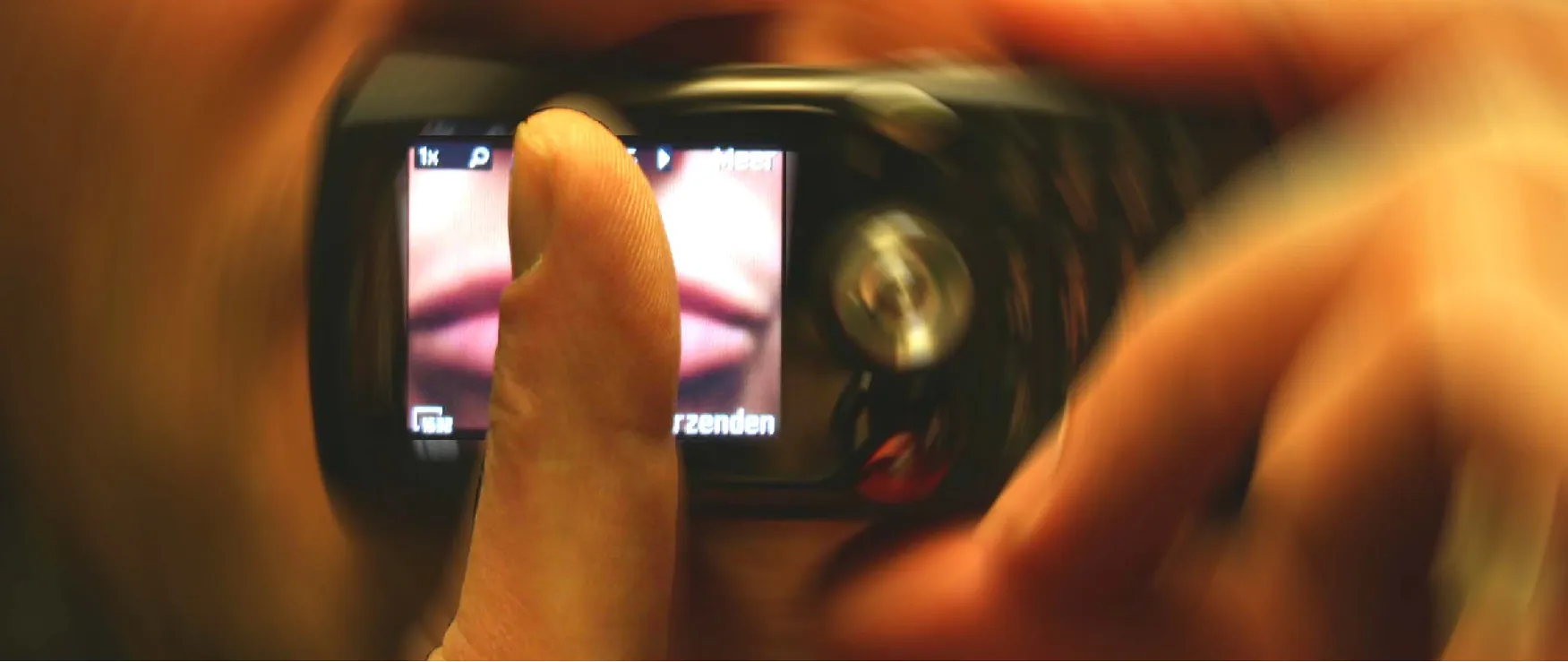 A person holding a phone with an image of lips over their own lips and then holding a finger over that image as if hushing someone. 